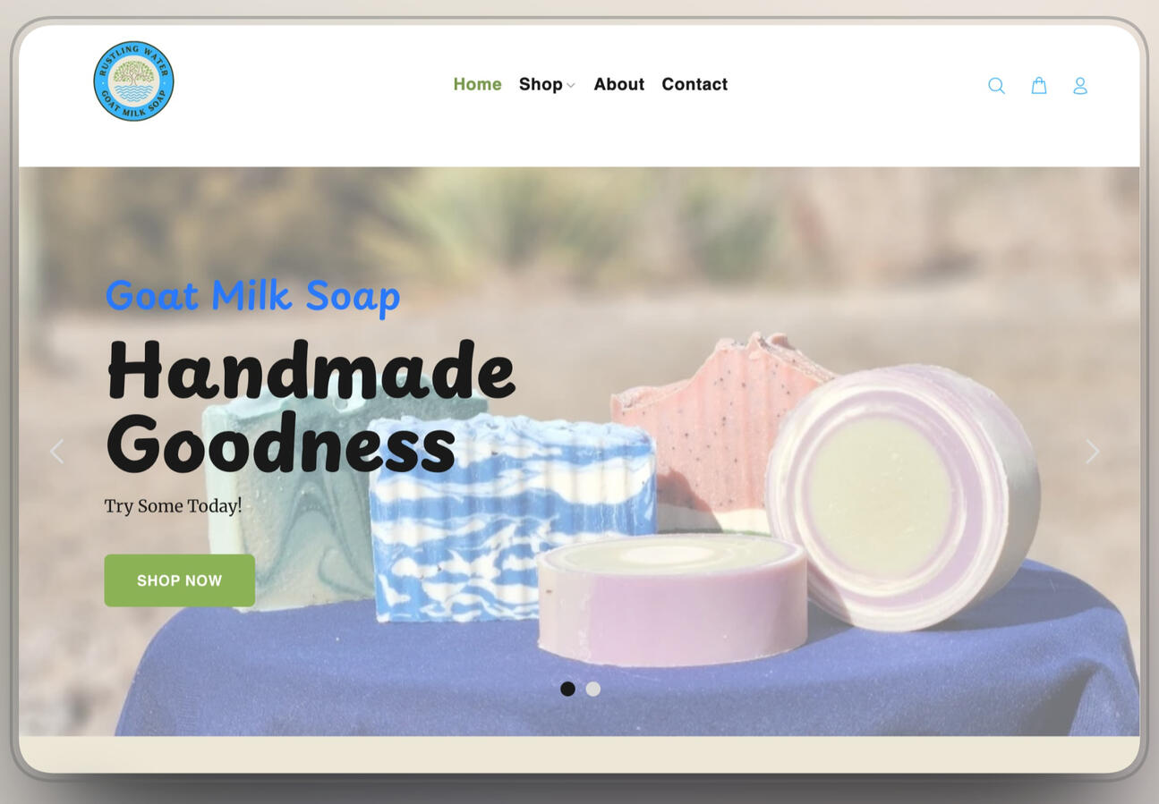 Homepage design for Rustling Water Goat Milk Soap, featuring a bright, outdoor aesthetic. Key elements include a hero image of colorful handmade soap bars displayed on a blue cloth against a blurred nature background, the headline "Handmade Goodness", and